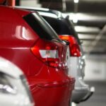 coche rojo aparcado junto a coche blanco y coche gris dentro de un garaje cerrado